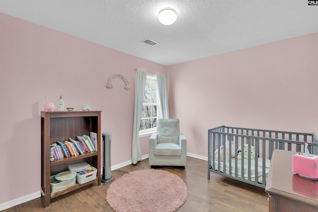 bedroom with wood-type flooring, a textured ceiling, and a crib