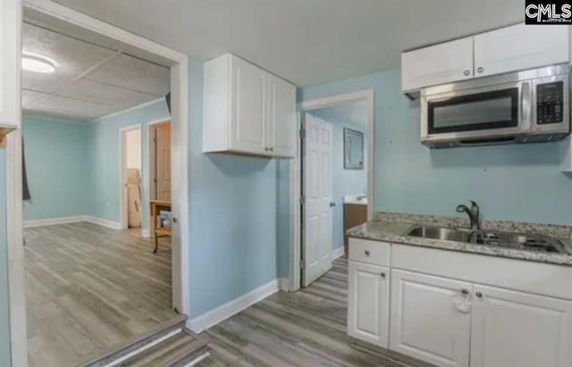 kitchen featuring light stone counters, sink, white cabinets, and light wood-type flooring