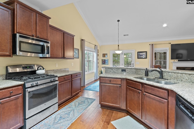 kitchen with sink, hanging light fixtures, stainless steel appliances, light stone counters, and vaulted ceiling