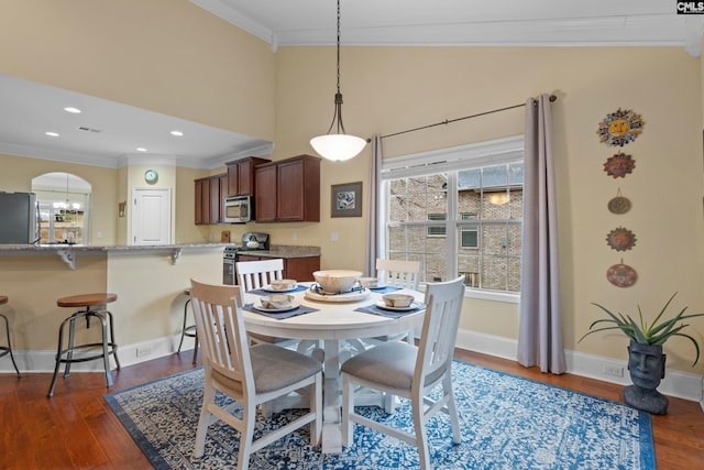 dining space with dark wood-type flooring, ornamental molding, and a high ceiling