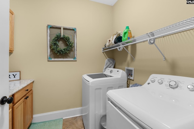 clothes washing area featuring separate washer and dryer, light tile patterned floors, and cabinets