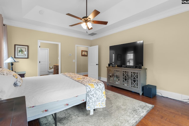 bedroom with dark wood-type flooring, ceiling fan, ensuite bathroom, ornamental molding, and a raised ceiling