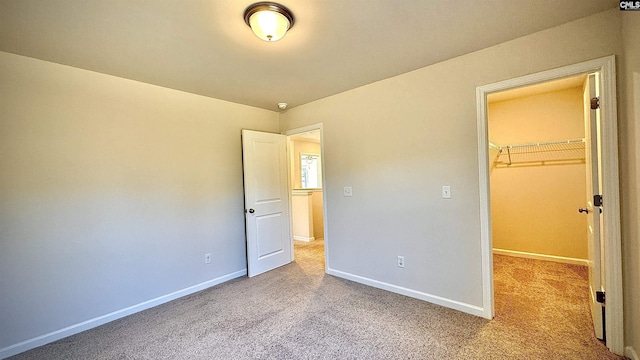 unfurnished bedroom featuring a walk in closet, a closet, and light carpet