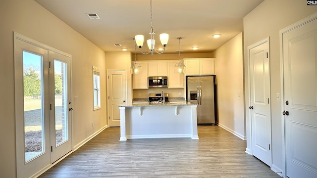 kitchen featuring stone countertops, a breakfast bar area, white cabinets, stainless steel appliances, and a center island with sink