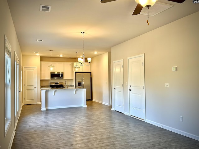 kitchen with decorative light fixtures, a breakfast bar area, white cabinets, a kitchen island with sink, and stainless steel appliances