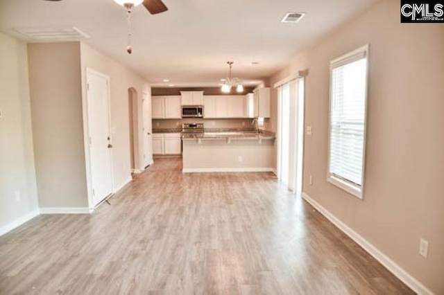 kitchen with appliances with stainless steel finishes, ceiling fan with notable chandelier, white cabinetry, hanging light fixtures, and light hardwood / wood-style floors