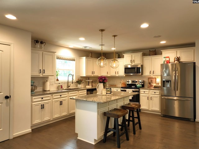 kitchen with sink, white cabinetry, appliances with stainless steel finishes, a kitchen island, and pendant lighting