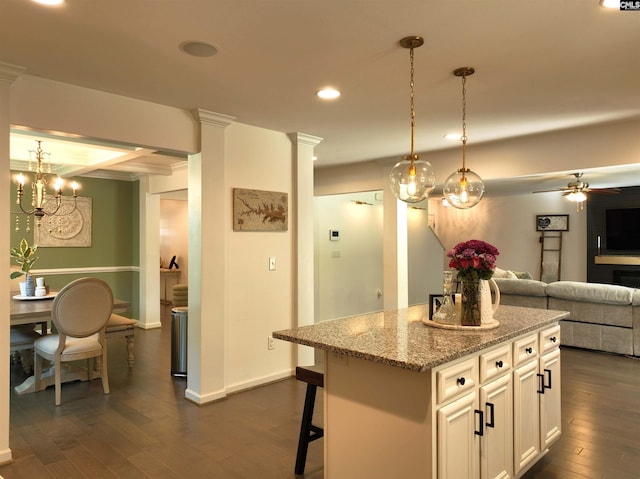 kitchen with a breakfast bar, decorative light fixtures, a kitchen island, light stone countertops, and white cabinets