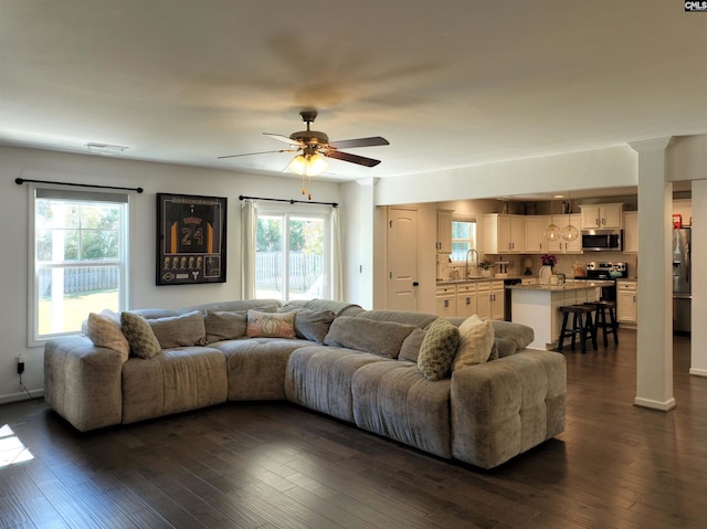 living room featuring ornate columns, dark wood-type flooring, sink, and ceiling fan