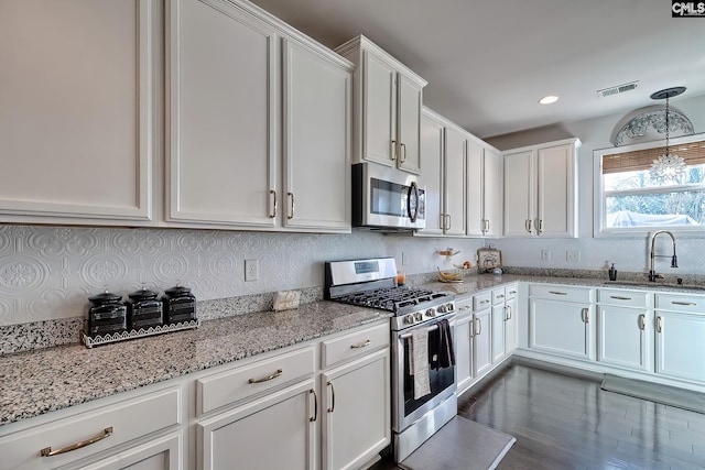 kitchen with stainless steel appliances, light stone countertops, sink, and white cabinets