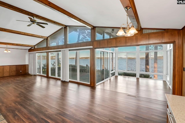 unfurnished living room with dark wood-type flooring, a water view, lofted ceiling with beams, ceiling fan with notable chandelier, and wood walls