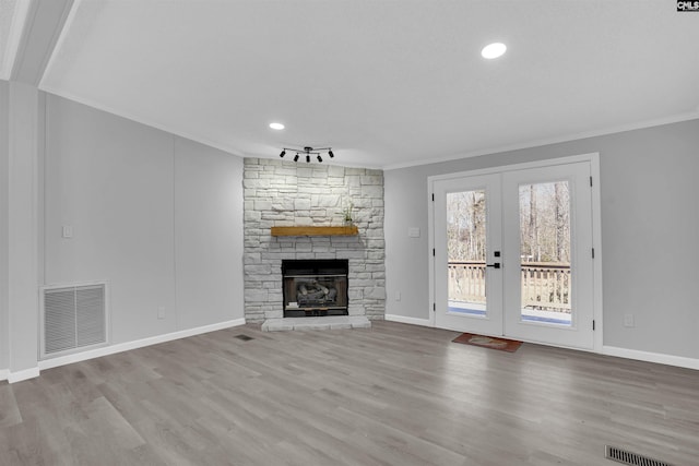 unfurnished living room featuring a fireplace, ornamental molding, french doors, and light wood-type flooring