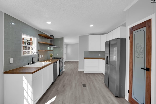 kitchen with sink, light hardwood / wood-style flooring, wooden counters, stainless steel appliances, and white cabinets