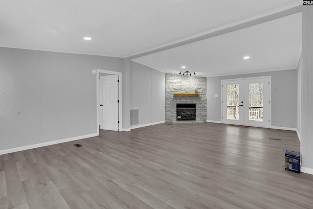 unfurnished living room with crown molding, a textured ceiling, a stone fireplace, french doors, and light wood-type flooring