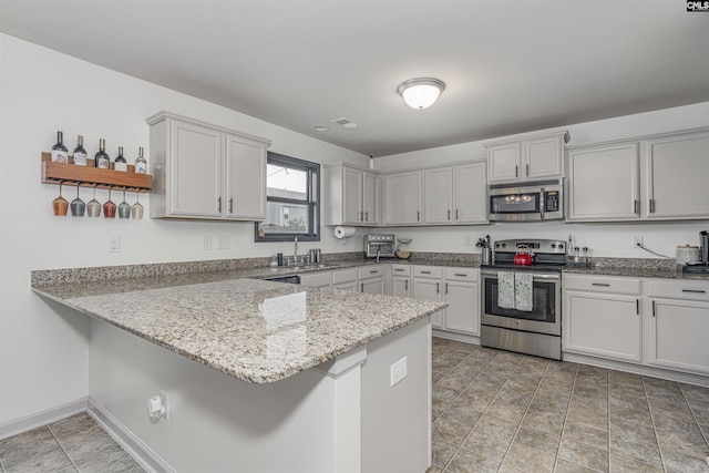 kitchen featuring sink, appliances with stainless steel finishes, kitchen peninsula, light stone countertops, and white cabinets