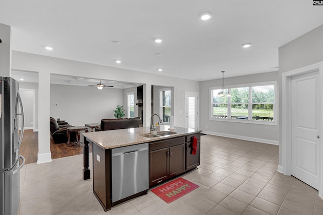 kitchen with sink, light stone counters, hanging light fixtures, appliances with stainless steel finishes, and an island with sink