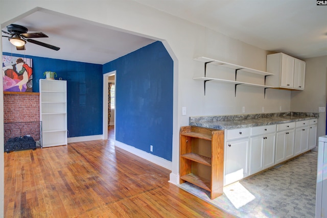 kitchen featuring ceiling fan, a fireplace, white cabinets, and light wood-type flooring