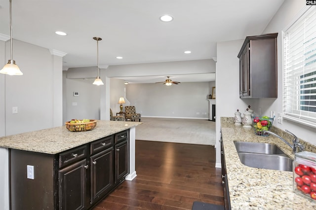 kitchen featuring dark brown cabinetry, sink, hanging light fixtures, dark hardwood / wood-style floors, and light stone countertops