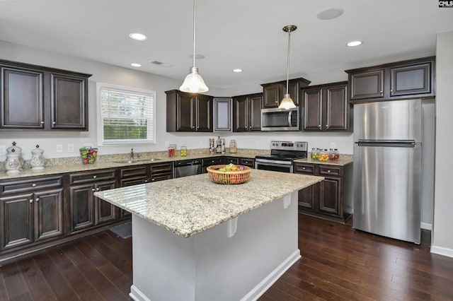 kitchen featuring stainless steel appliances, decorative light fixtures, sink, and a kitchen island