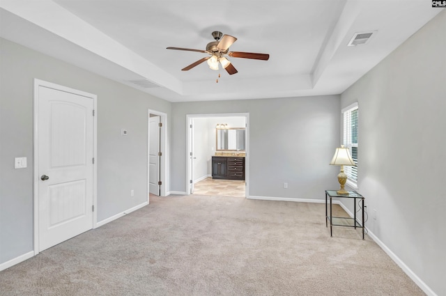 spare room featuring a tray ceiling, light colored carpet, and ceiling fan