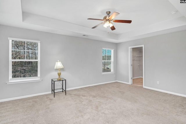 carpeted empty room with ceiling fan and a raised ceiling