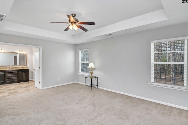 unfurnished bedroom with light carpet, a tray ceiling, and ensuite bath