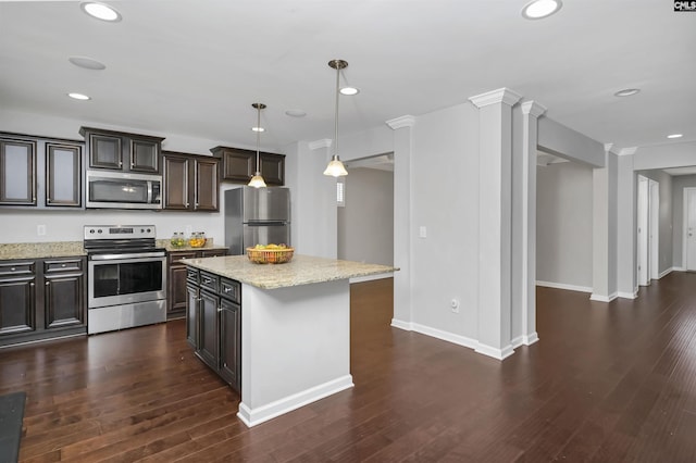 kitchen with dark wood-type flooring, light stone counters, appliances with stainless steel finishes, a kitchen island, and pendant lighting