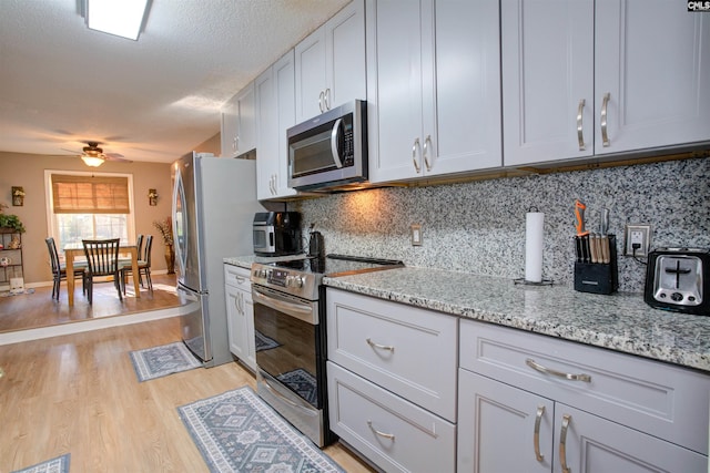 kitchen featuring light stone counters, tasteful backsplash, light wood-type flooring, appliances with stainless steel finishes, and ceiling fan