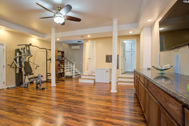 exercise area with dark hardwood / wood-style flooring, a wall unit AC, and decorative columns