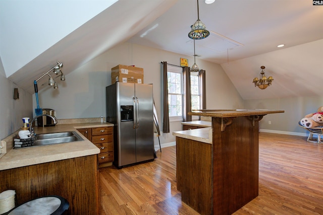 kitchen featuring pendant lighting, lofted ceiling, stainless steel fridge, light hardwood / wood-style flooring, and a kitchen bar