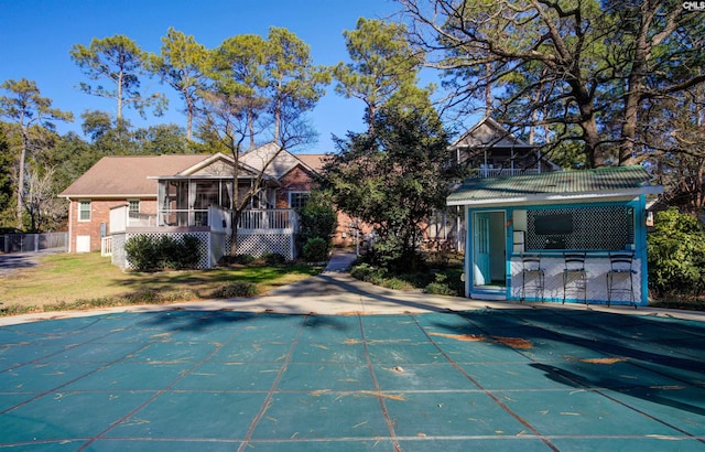 back of property featuring a sunroom, a covered pool, a lawn, and a bar