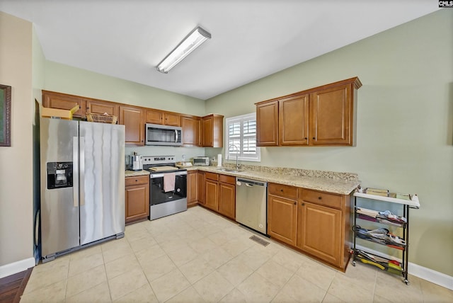 kitchen featuring appliances with stainless steel finishes, sink, and light stone counters