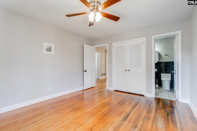 unfurnished bedroom featuring connected bathroom, tile walls, a closet, hardwood / wood-style flooring, and ceiling fan