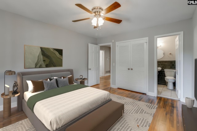 bedroom with hardwood / wood-style floors, tile walls, ceiling fan, ensuite bath, and a closet