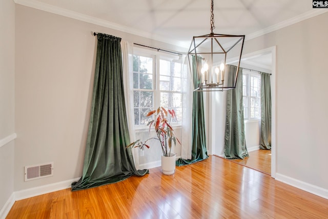 unfurnished dining area featuring wood-type flooring, ornamental molding, and a chandelier