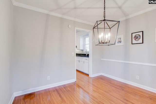 unfurnished dining area featuring sink, crown molding, wood-type flooring, and a chandelier