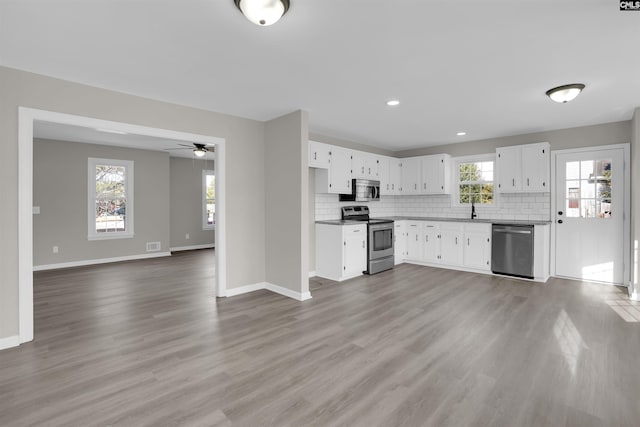 kitchen with appliances with stainless steel finishes, white cabinetry, backsplash, ceiling fan, and light hardwood / wood-style flooring