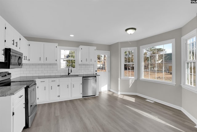 kitchen with white cabinetry, stainless steel appliances, light stone countertops, and sink