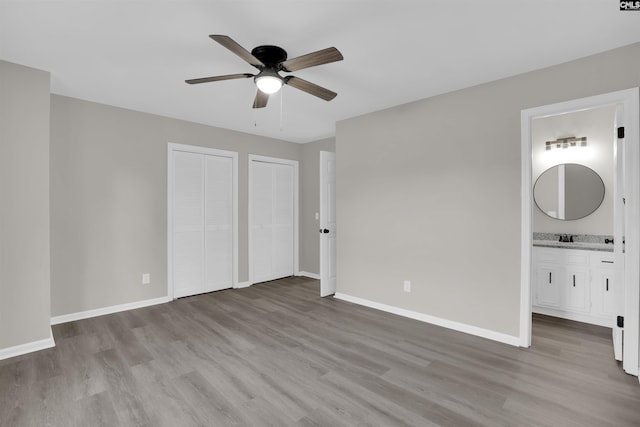 unfurnished bedroom featuring two closets, sink, ceiling fan, light hardwood / wood-style floors, and ensuite bath