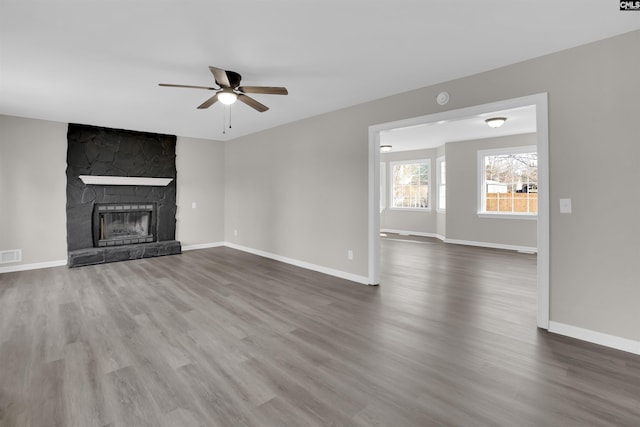 unfurnished living room featuring a stone fireplace, dark wood-type flooring, and ceiling fan