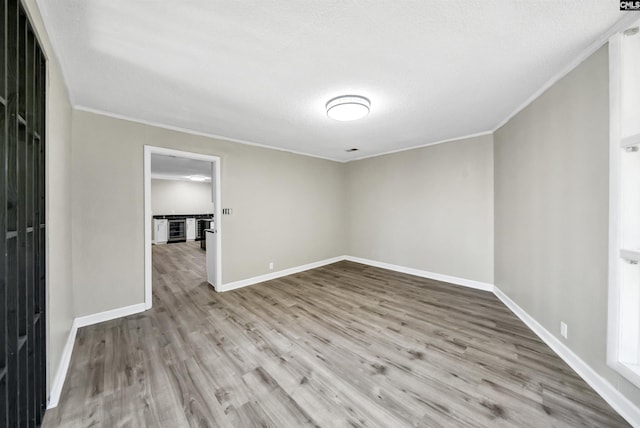 empty room with ornamental molding, light hardwood / wood-style floors, and a textured ceiling