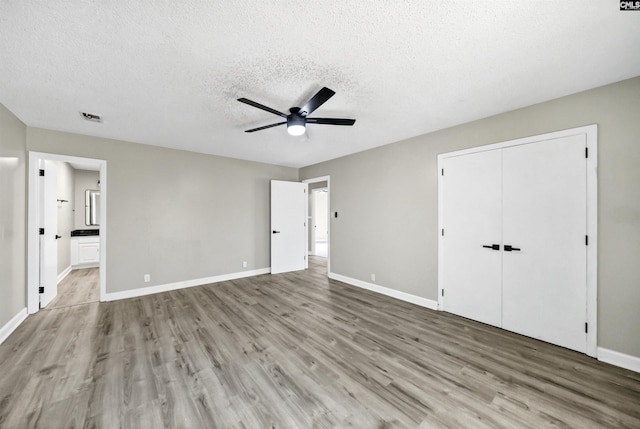 unfurnished bedroom featuring ensuite bathroom, light hardwood / wood-style flooring, ceiling fan, a textured ceiling, and a closet