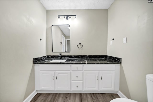 bathroom featuring vanity, a textured ceiling, wood-type flooring, and toilet