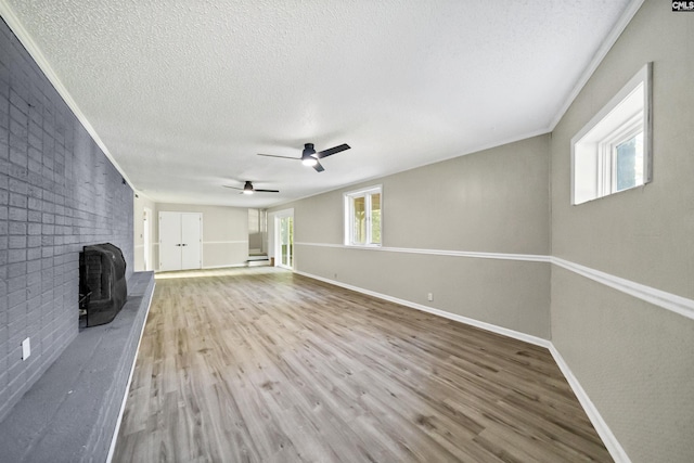 unfurnished living room featuring a brick fireplace, crown molding, wood-type flooring, and a textured ceiling