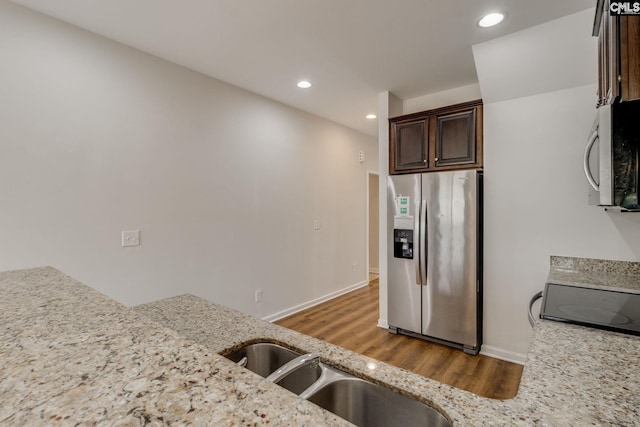 kitchen with appliances with stainless steel finishes, wood-type flooring, sink, dark brown cabinetry, and light stone counters