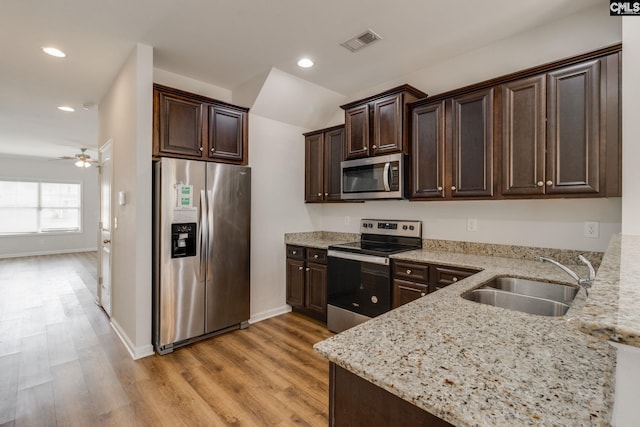 kitchen with sink, appliances with stainless steel finishes, dark brown cabinets, light stone counters, and light wood-type flooring