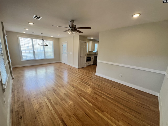 unfurnished living room featuring ceiling fan with notable chandelier and light hardwood / wood-style floors