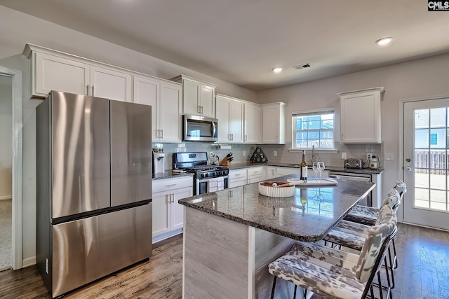 kitchen featuring a breakfast bar area, appliances with stainless steel finishes, white cabinetry, dark stone countertops, and a center island