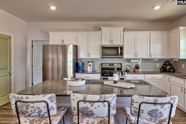 kitchen featuring dark stone countertops, stainless steel appliances, white cabinets, a kitchen island, and decorative backsplash