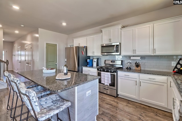 kitchen with appliances with stainless steel finishes, a breakfast bar, white cabinets, and dark stone counters